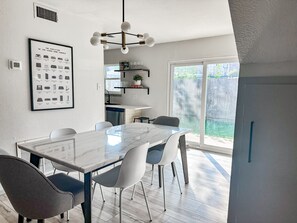 A modern kitchen with a dining area, featuring a marble table, white chairs, and a pendant light. - Gamer's Day Den - Walk to Kyle Field (College Station)