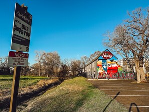 A bus stop sign with a welcome sign for Aggieland, a grassy area, and a building with a mural. - Gamer's Day Den - Walk to Kyle Field (College Station)
