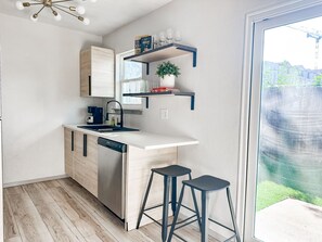 A compact kitchen with a dishwasher, a coffee machine, and a small bar stool. - Gamer's Day Den - Walk to Kyle Field (College Station)