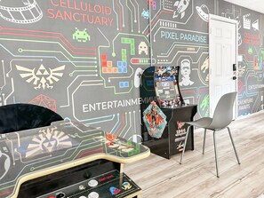 A room with a retro gaming console, a white door, and a wall with entertainment-themed graphics. - Gamer's Day Den - Walk to Kyle Field (College Station)