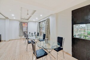 Uma sala de conferências com mesa e cadeiras de vidro, paredes brancas e uma grande janela com cortinas estampadas.