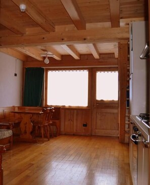A wooden interior with a dining table, chairs, a refrigerator, and a window.