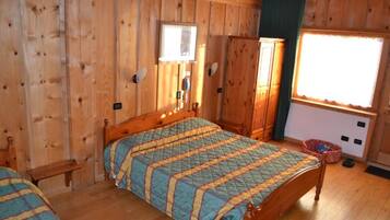 Una stanza con rivestimenti in legno, un letto, una panca, un armadio e una finestra.
