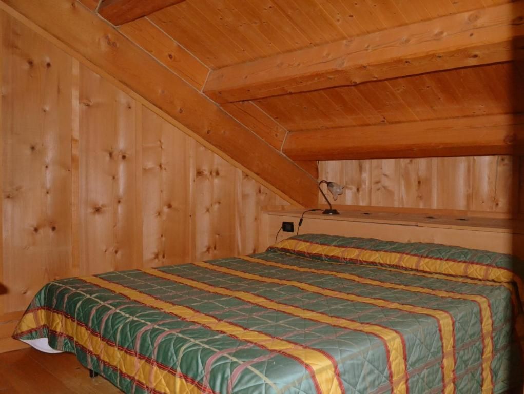 Una habitación con techo de madera inclinado y una cama con colcha verde y amarilla.