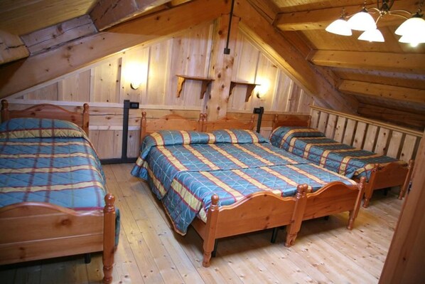 A room with three wooden beds arranged in a row, wooden walls, and a sloped ceiling with light fixtures.