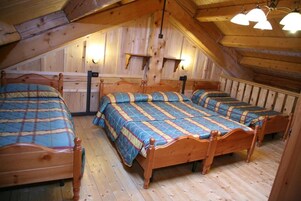 Una habitación con tres camas de madera alineadas, paredes de madera y un techo inclinado con luminarias.
