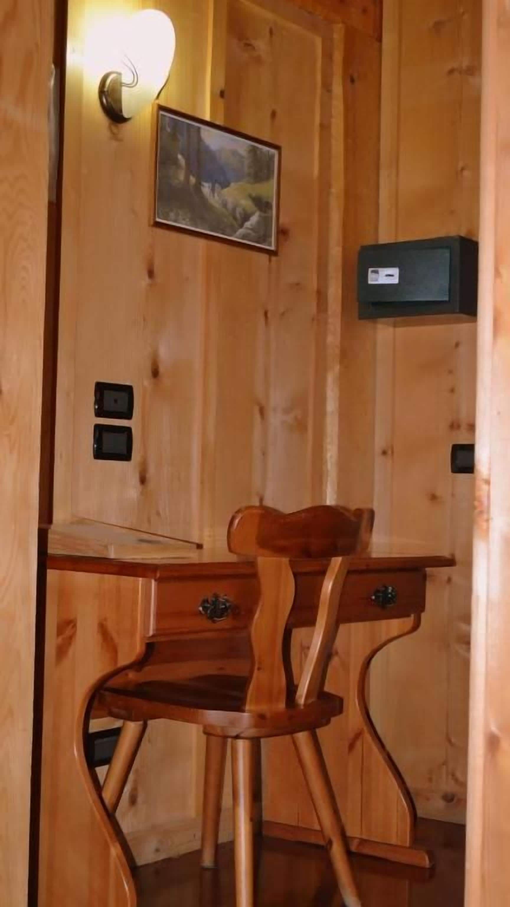 Interior de una cabaña de madera con un escritorio, una silla, una lámpara de pared y un cuadro enmarcado.