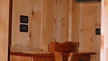 Interior de una cabaña de madera con un escritorio, una silla, una lámpara de pared y un cuadro enmarcado.