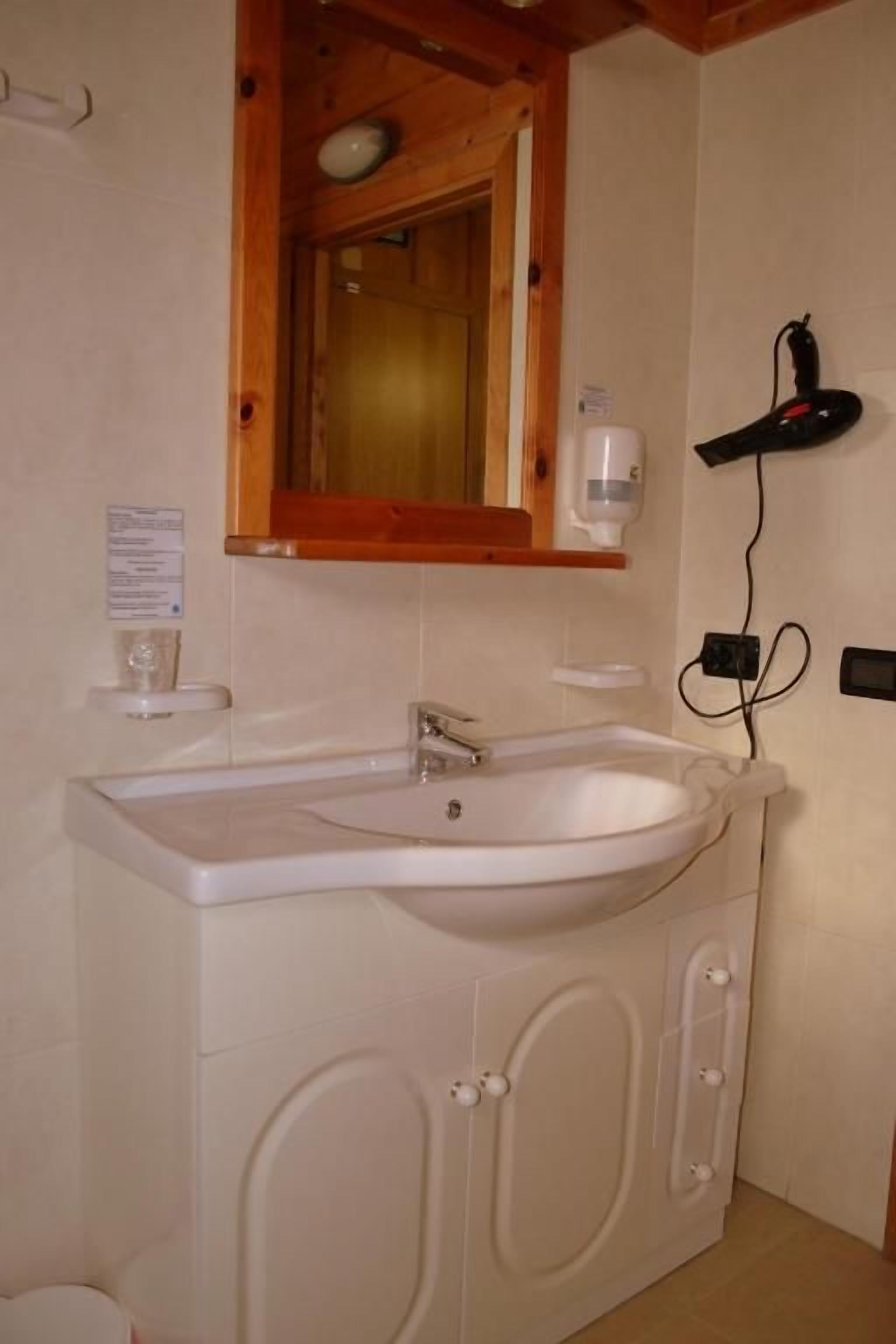 A bathroom with a white sink, wooden cabinet, and a mirror with a wooden frame.
