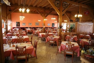 Un restaurante con varias mesas y sillas, vigas de madera en el techo y cuadros en las paredes.