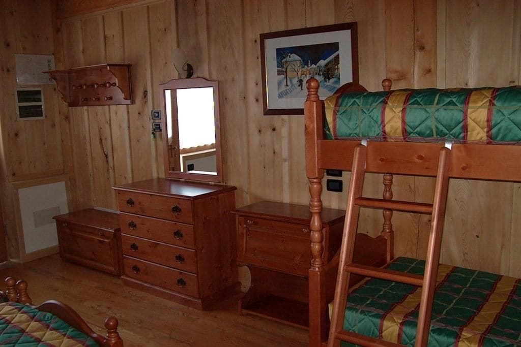 A wooden room with a bunk bed, a dresser, a mirror, and a framed picture on the wall.