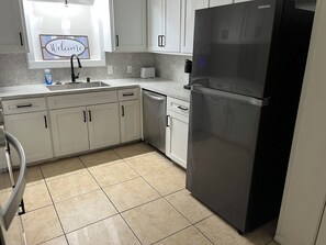 A kitchen with white cabinets, a stainless steel refrigerator, a dishwasher, and a window with a welcome sign. - Beautiful 4-bedroom house in enchanting West Orange with AC (West Orange)
