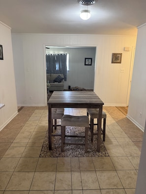 A dining area with a wooden table and four upholstered chairs. The room has white paneled walls and a tiled floor with a mix of large and small tiles. - Beautiful 4-bedroom house in enchanting West Orange with AC (West Orange)