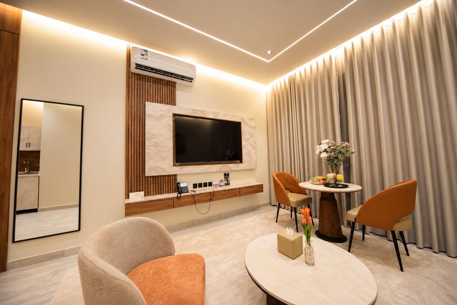 A modern hotel room with a flat-screen TV, a desk with a telephone, and a dining area with two chairs and a table.