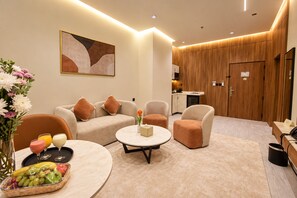 A modern hotel room with a sofa set, a coffee table, a fruit basket, and a painting on the wall.
