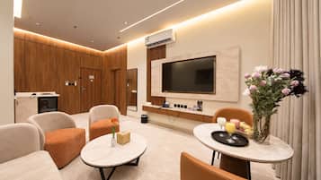 A modern hotel room with a flat-screen TV, comfortable seating, a small table with a vase of flowers, and a minibar.