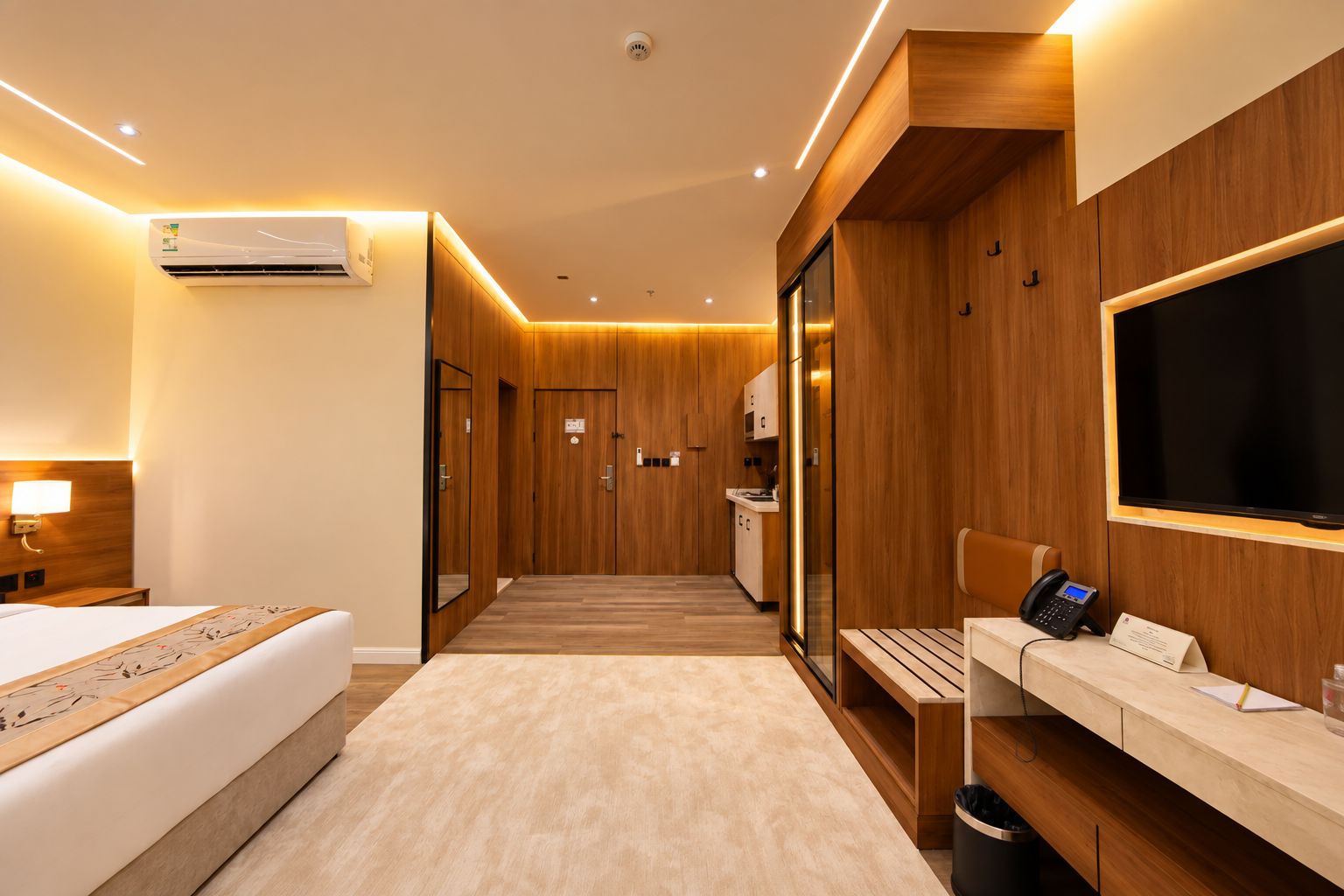 A hotel room with a bed, bedside table, desk with a computer, and a TV.