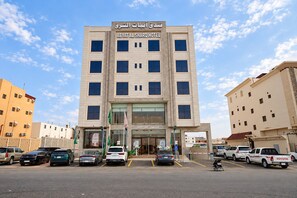 A hotel with a reception at the ground level, multiple floors, and a parking lot with various vehicles. - Abyat Alsharq Hotel (Madinah)