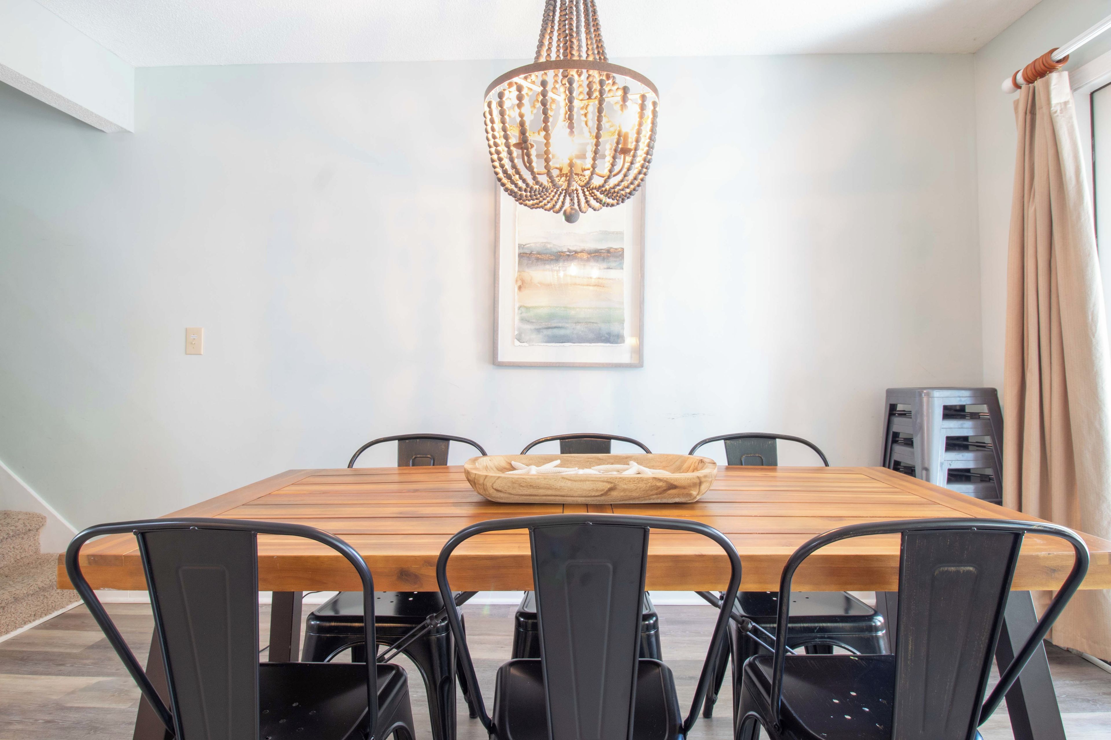 A dining area with a wooden table, black chairs, a chandelier, and a painting on the wall.
