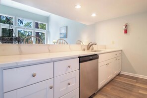 A kitchen with white cabinetry, a dishwasher, a sink, and a window with a view of trees. - 3 Bedroom Townhome- With Resort Access (Edisto Island)