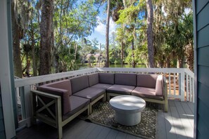 A covered outdoor seating area with a sectional sofa and a round table, surrounded by a white railing, overlooking a body of water and dense trees. - 3 Bedroom Townhome- With Resort Access (Edisto Island)