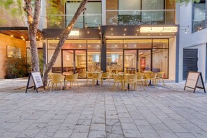 Ein Café mit Außenbereich, einer Schautafel und einem Baum davor.
