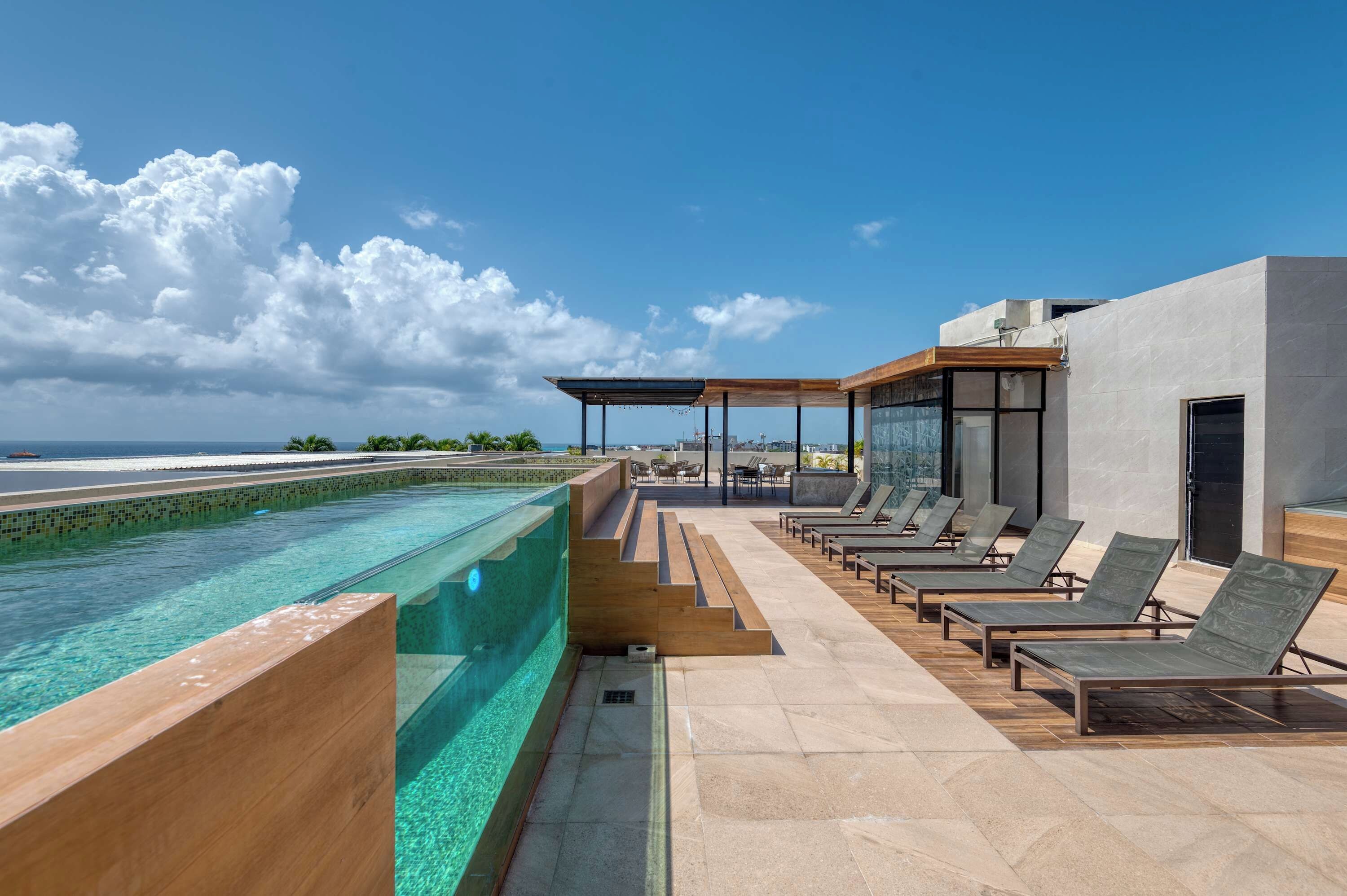 A rooftop pool area with clear blue water, lounge chairs, and a view of the ocean.