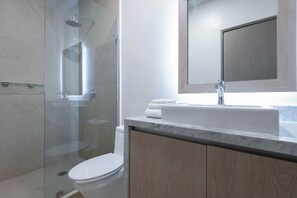 Une salle de bain moderne avec une douche à parois de verre, des toilettes blanches et un plan de toilette en marbre avec un lavabo et un miroir.