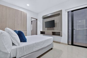 Une chambre à coucher moderne avec un lit, un téléviseur fixé au mur et une porte-fenêtre coulissante.
