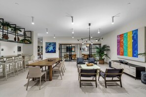 A spacious dining area with a long wooden table and multiple chairs, a modern kitchen with a large colorful painting, and a ceiling with multiple light fixtures. - District 225 unit 3202 -Miami Highline & Resort (Miami)