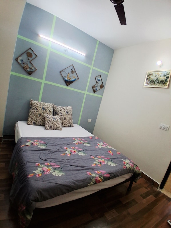 Una camera da letto con un letto, una coperta a fiori, decorazioni murali e una ventola a soffitto.