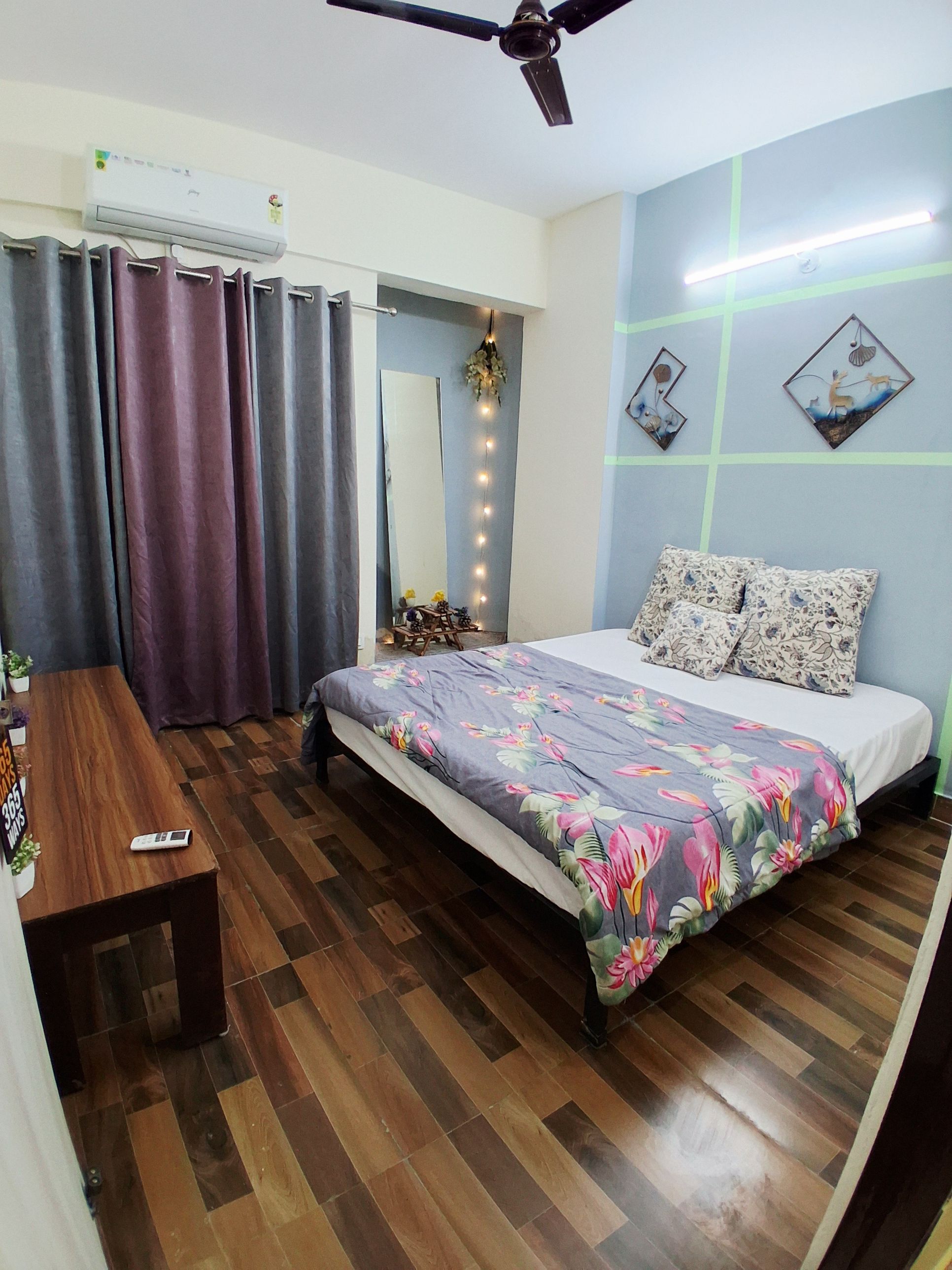 A bedroom with a bed, a wooden table, a ceiling fan, and a wall-mounted air conditioner.