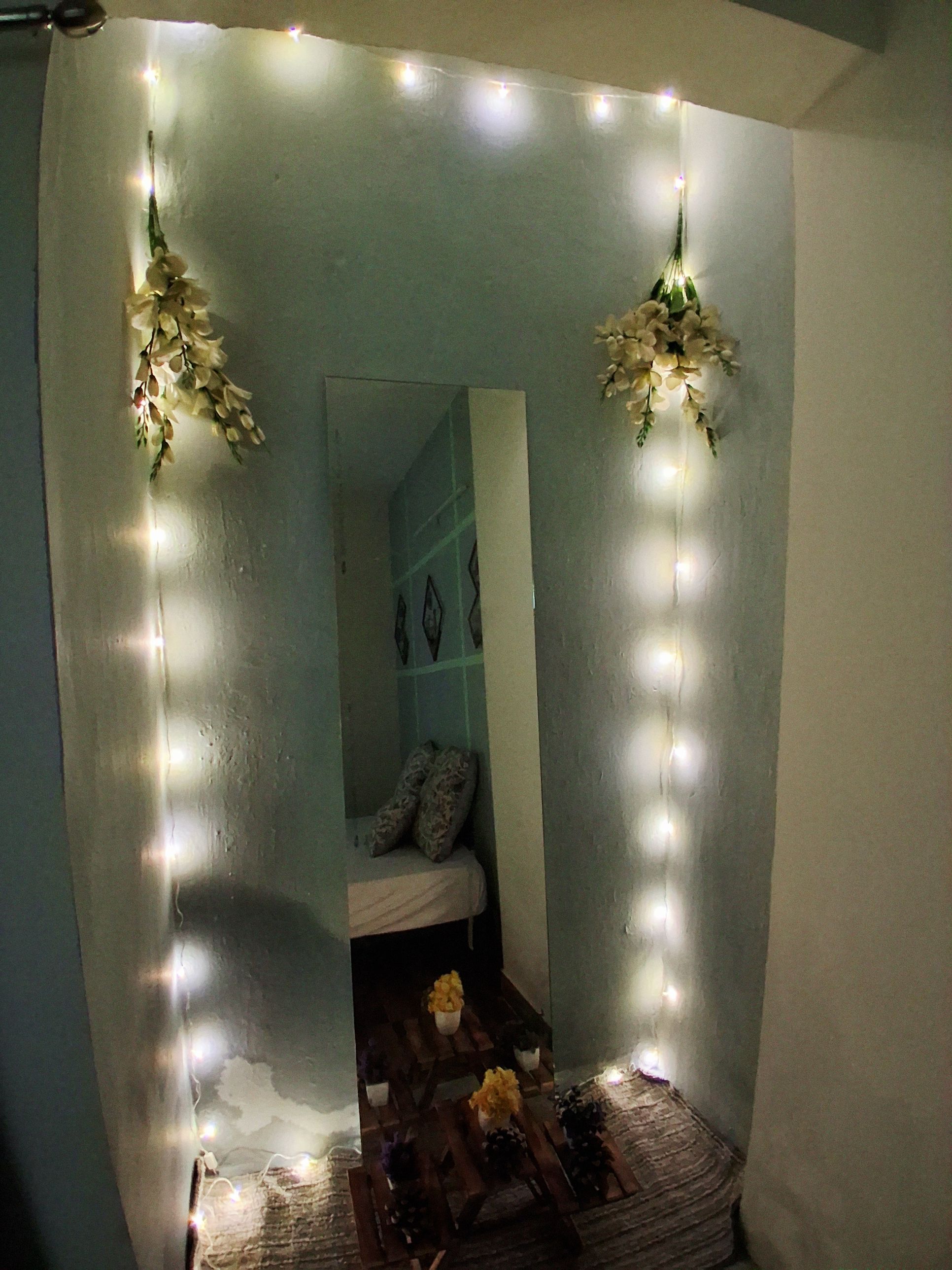 Une chambre avec un lit, une petite table décorée de fleurs et des guirlandes lumineuses.