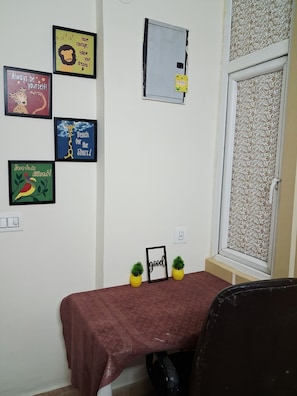 Una stanza con un tavolo, poster motivazionali appesi, una finestra con tende a fantasia e una porta con serratura.