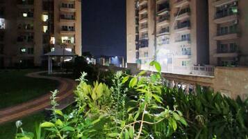 Una vista notturna di un edificio residenziale con numerosi balconi, un giardino curato in primo piano e un vialetto lastricato.