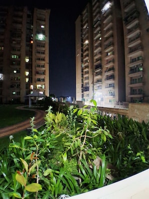 Una vista notturna di un edificio residenziale con numerosi balconi, un giardino curato in primo piano e un vialetto lastricato.