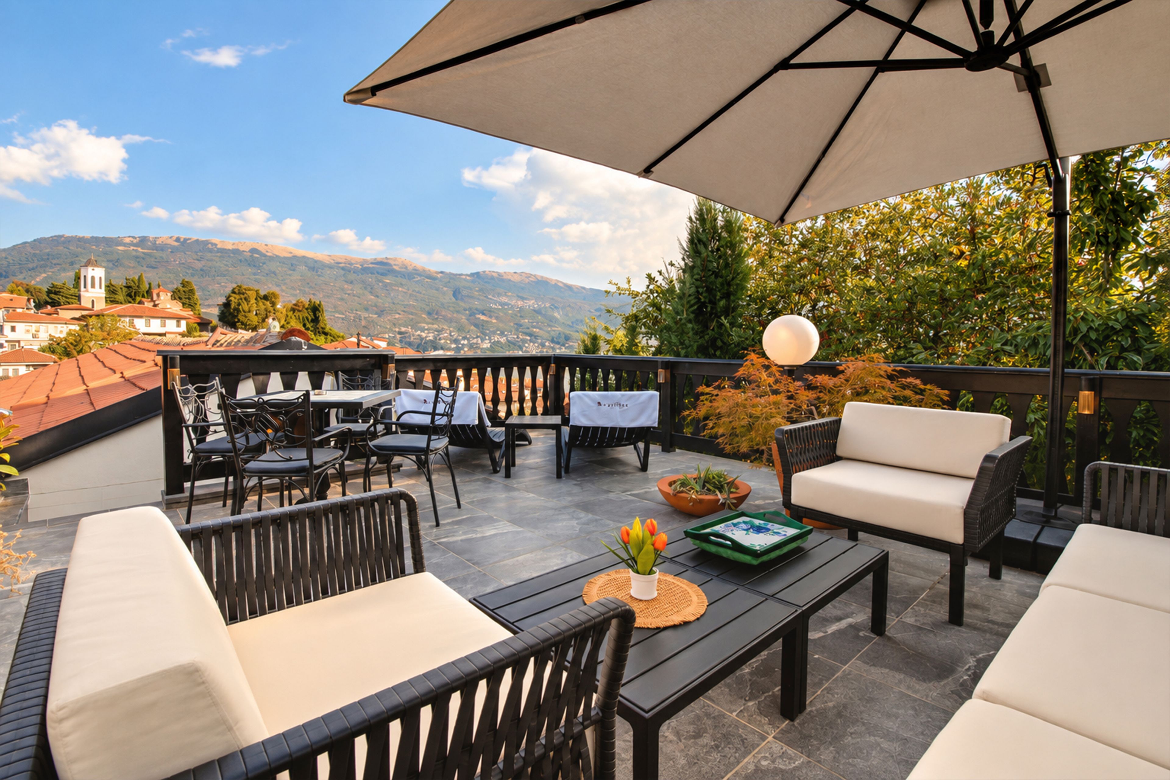 A terrace with outdoor furniture, a table, and a view of a mountain and town.