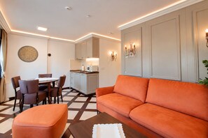 A modern living room with a sofa, ottoman, and dining area with chairs. - Villa Amfitea (Ohrid)