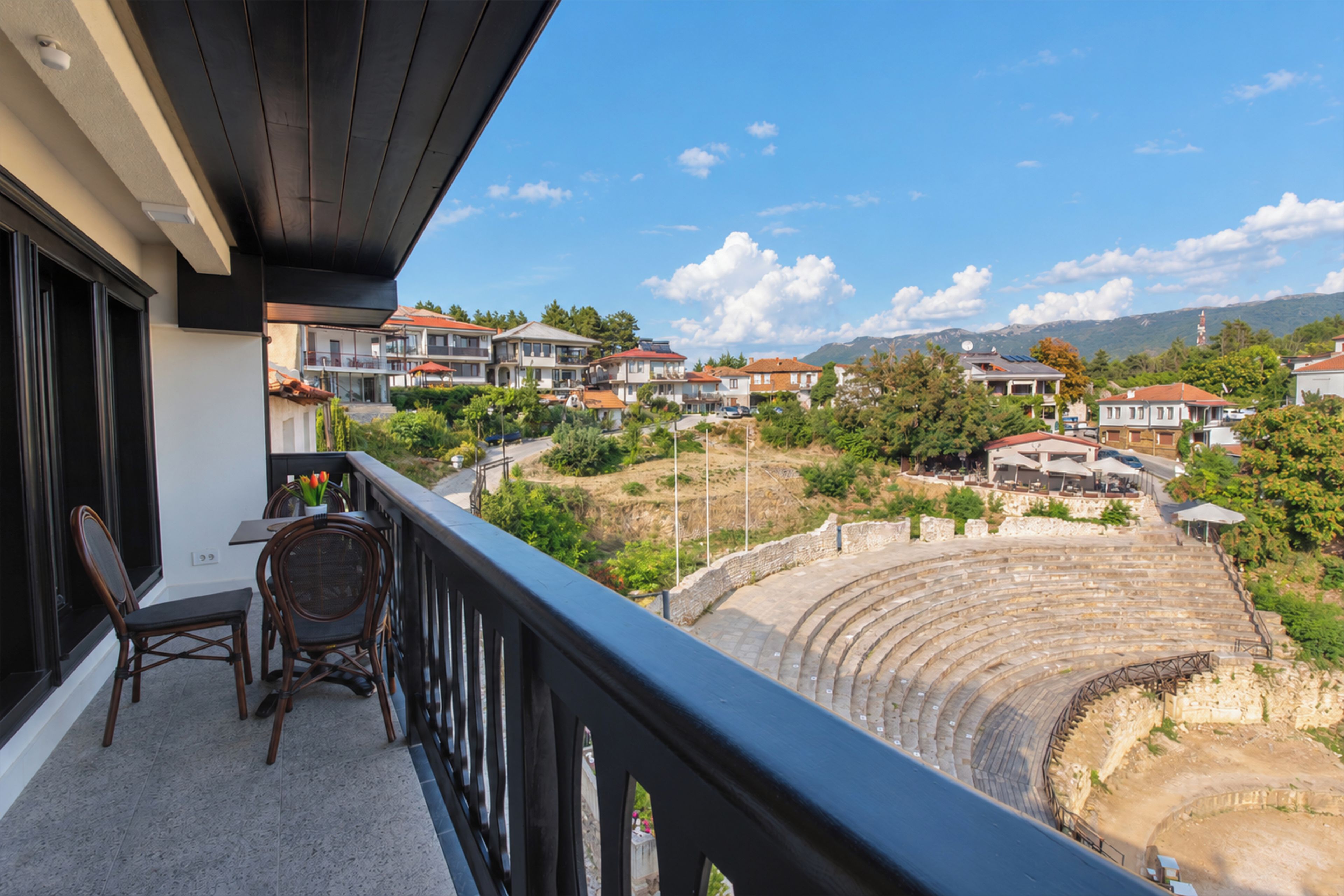 A balcony with a view of a residential area and an ancient amphitheater.