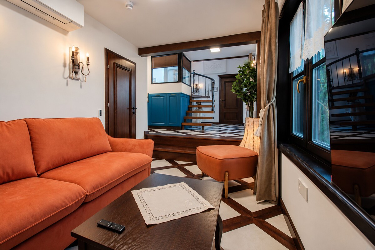A living room with a sofa, a coffee table, and a view of a staircase leading to a bedroom.