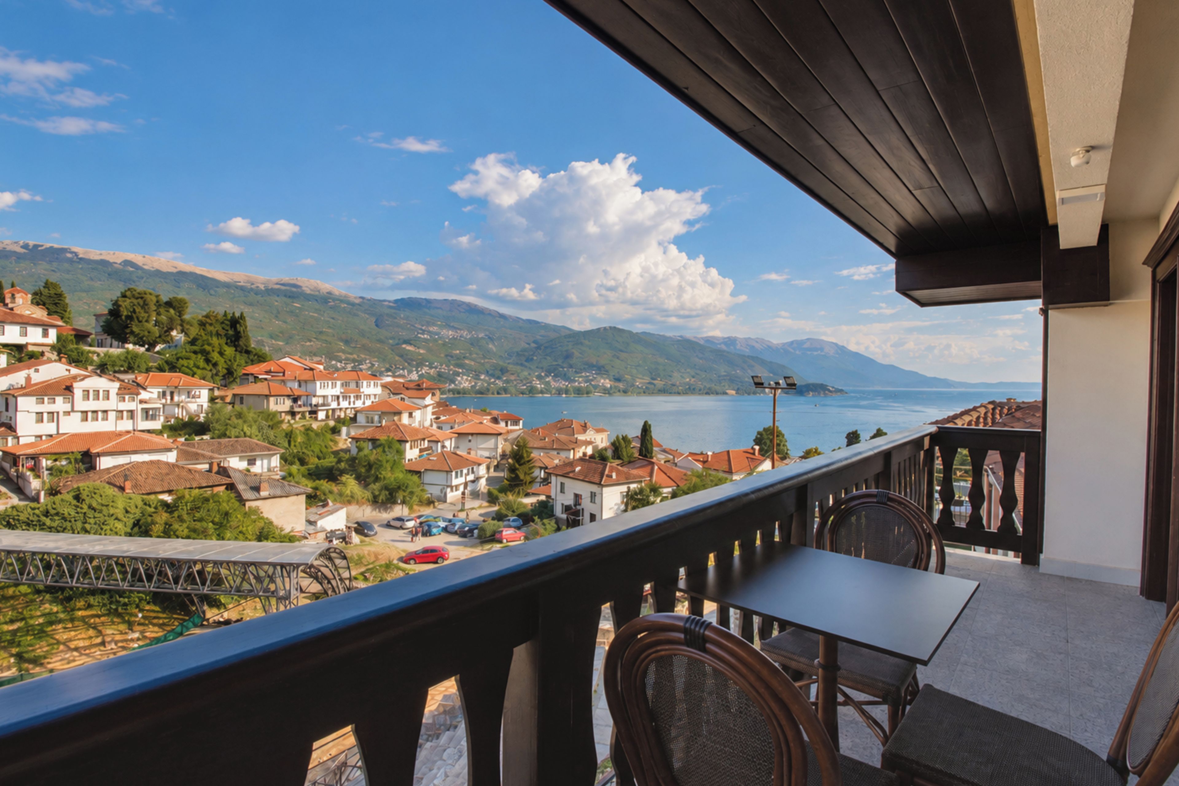 A balcony with a view of a lake and mountains, wooden furniture, and a clear sky.