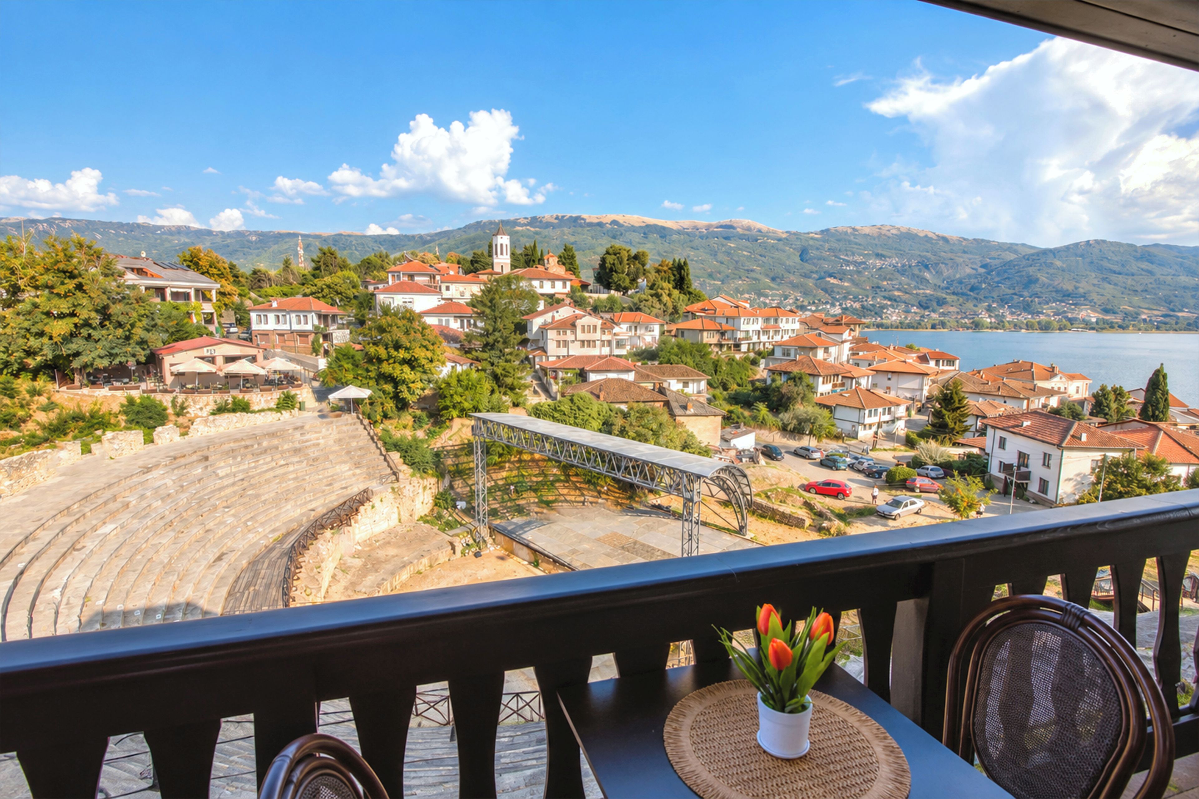 En balkon med udsigt over en kystby, en scene og et bjerglandskab i baggrunden.