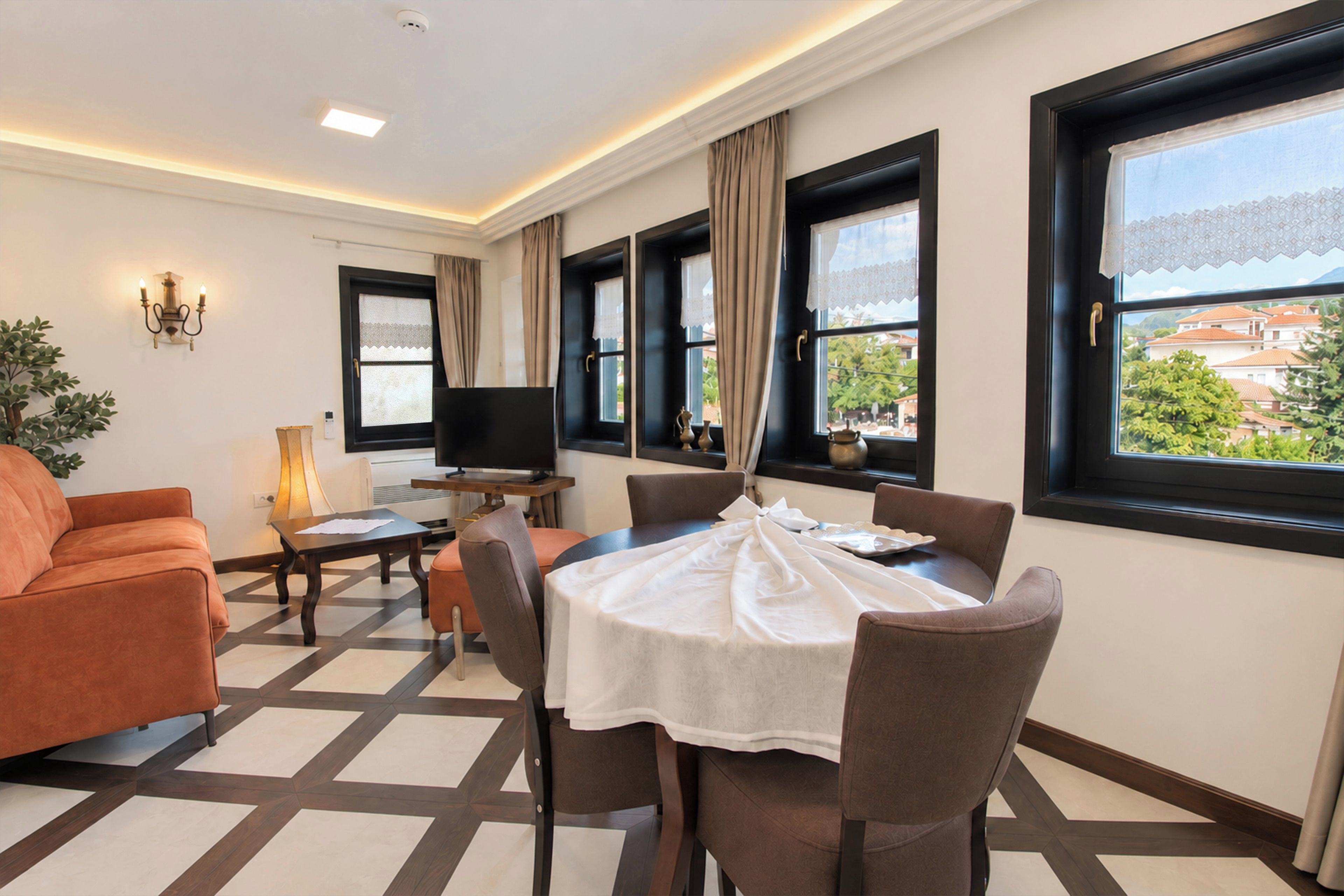 Una camera d'albergo con zona pranzo, divano, televisione e ampie finestre vista.