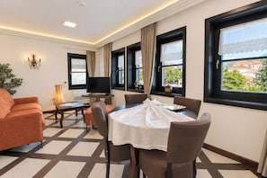 A hotel room with a dining area, a sofa, a television, and large windows with a view.