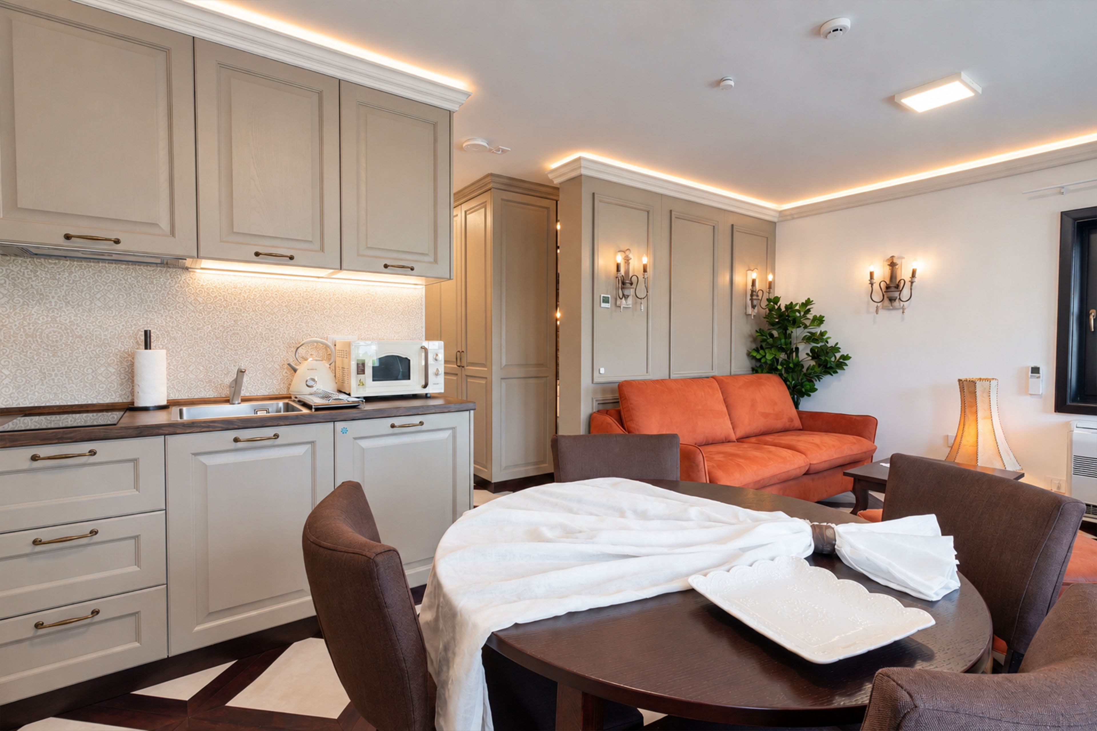 Et moderne køkken med indbyggede apparater, et spiseområde med et rundt bord og stole, og en stue med en orange sofa.