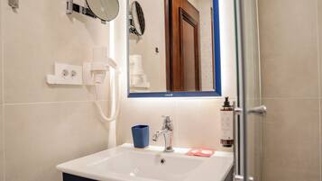 Un baño con un lavamanos blanco, un espejo, una taza azul y una puerta de ducha.