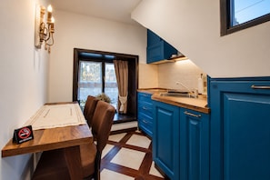 A compact kitchen with blue cabinets, a wooden dining table, and a view through the window.