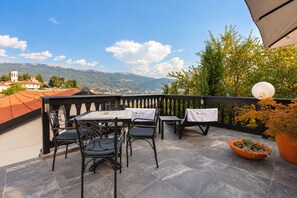 A terrace with a table and chairs, a potted plant, and a view of mountains and a church.