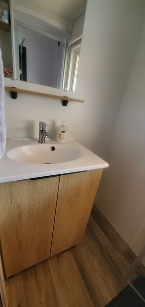A bathroom with a white sink, wooden cabinets, a mirror, and a towel. - Mobile home with direct beach access (Canet-en-Roussillon)