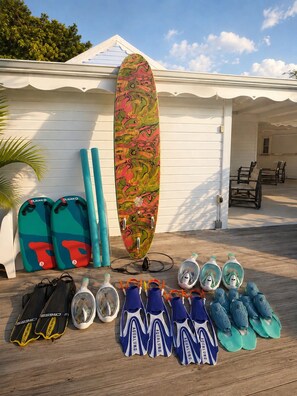 A surfboard, two pairs of swim fins, and a set of snorkels and flippers on a wooden deck. - Villa Azura – 4 Bedrooms, Infinity Pool, Spa & Surf | Le Helleux (Sainte-Anne)